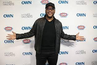 A man smiling and posing on a red carpet with arms open wide.